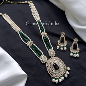 May include: An ornate necklace and earring set. The necklace features white and green beads, with a large pendant and floral accents. The earrings have black stone centers and pearl drops. The set is displayed on a black and white background.
