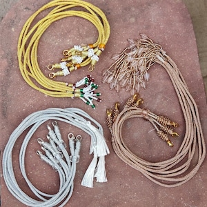 May include: Four strands of cord with decorative tassels. The cords are gold, silver, brown, and clear with beads.