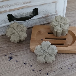 Könnte beinhalten: Drei grüne und weiße seifenförmige Blumen. Zwei der Seifen liegen auf einem Seifenablage aus Holz. Die dritte Seife liegt auf einer Holzoberfläche.