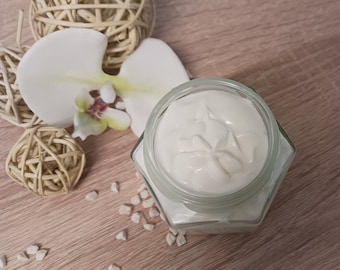 Peut inclure: Une crème blanche dans un pot en verre transparent avec une base hexagonale. Le pot est posé sur une surface en bois avec des pierres décoratives blanches et une orchidée blanche.