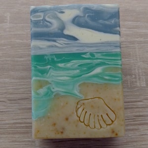 Puede incluir: Una pastilla de jab&oacute;n con un dise&ntilde;o de concha marina. El jab&oacute;n est&aacute; en capas con remolinos azules, verdes y blancos, que se asemejan a una escena de playa.