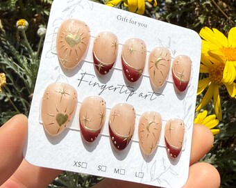 May include: A set of press-on nails with a nude base, gold accents, and a deep red French tip. Designs include suns, stars, and moons. The card reads "Gift for you" and "Fingertip art". Sizes XS, S, M, and L are indicated.