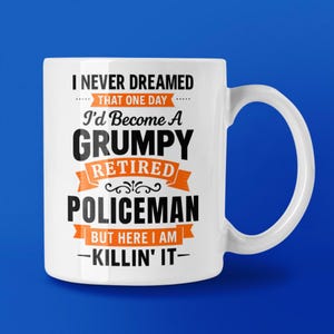 May include: White ceramic mug with the text "I NEVER DREAMED THAT ONE DAY I'd Become A GRUMPY RETIRED POLICEMAN BUT HERE I AM -KILLIN' IT-" in black and orange lettering. The mug has a curved handle and is set against a blue background.