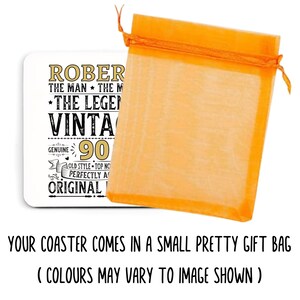 May include: A white coaster with gold and black text, including "ROBERT", "VINTAGE", and "90". It is packaged in an orange organza gift bag. The coaster is a vintage-themed gift.