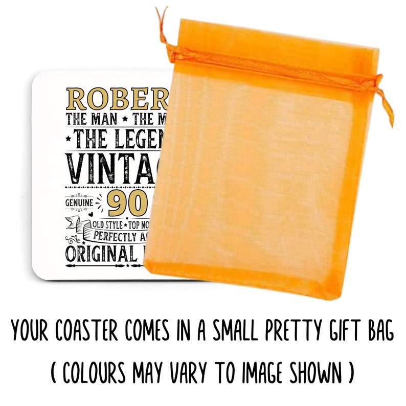 May include: A white coaster with gold and black text, including "ROBERT", "VINTAGE", and "90". It is packaged in an orange organza gift bag. The coaster is a vintage-themed gift.
