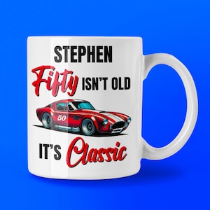 以下が含まれることがあります： 白いセラミックマグカップ。赤いスポーツカーのグラフィックと「STEPHEN Fifty ISN'T OLD IT'S Classic」の文字。車は赤と白のストライプで、ナンバー50。背景は青色。