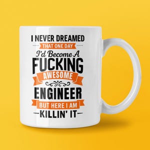 May include: White ceramic mug with a black and orange graphic that reads "I NEVER DREAMED THAT ONE DAY I'd Become A FUCKING AWESOME ENGINEER BUT HERE I AM - KILLIN' IT-". The mug has a curved handle and is set against a yellow background.
