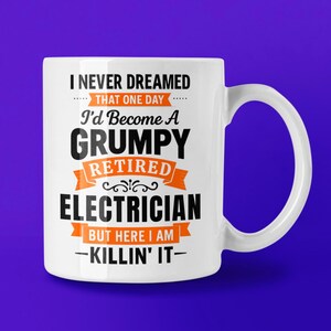 May include: White ceramic mug with the text "I NEVER DREAMED THAT ONE DAY I'd Become A GRUMPY RETIRED ELECTRICIAN BUT HERE I AM -KILLIN' IT-" in black and orange lettering. The mug has a curved handle and is set against a purple background.