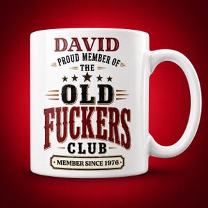 May include: A white ceramic mug featuring dark red and black text that reads DAVID PROUD MEMBER OF THE OLD FUCKERS CLUB MEMBER SINCE 1976. The design includes five stars above the word OLD and decorative horizontal lines throughout the graphic.