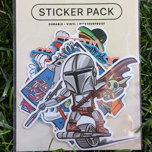 Könnte beinhalten: Eine Packung Aufkleber in einer transparenten Plastikhülle. Die Packung hat einen beigen Hintergrund mit den Worten "STICKER PACK" in einem schwarzen Oval. Die Aufkleber zeigen Cartoon-Charaktere und -Designs.