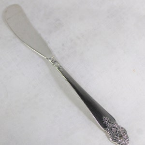 May include: A silver butter knife with an ornate handle. The handle has a floral design.