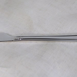 May include: A silver butter knife with a rounded blade and a decorative floral pattern on the handle. The knife is made of a shiny, reflective metal and is set against a white background.