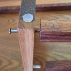 K&ouml;nnte beinhalten: Nahaufnahme eines Holzregals mit einer Metallschraube und einer wei&szlig;en Plastikkappe. Das Regal ist mit der Nummer "2" in einem Kreis gekennzeichnet.