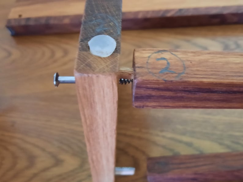 K&ouml;nnte beinhalten: Nahaufnahme eines Holzregals mit einer Metallschraube und einer wei&szlig;en Plastikkappe. Das Regal ist mit der Nummer "2" in einem Kreis gekennzeichnet.