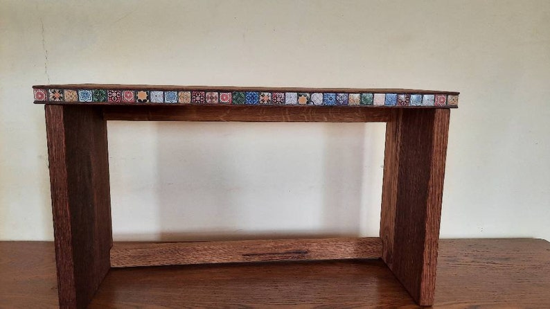 K&ouml;nnte beinhalten: Eine Holzbank mit einem dekorativen Fliesenrand. Die Bank ist aus dunklem Holz und hat ein schlichtes Design.