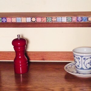 K&ouml;nnte beinhalten: Ein Holzregal mit einem dekorativen Fliesenrand, einem roten Pfefferm&uuml;hle, einer wei&szlig;en Teetasse mit blauem Blumendesign und einem roten Apfel auf einer Holzoberfl&auml;che.