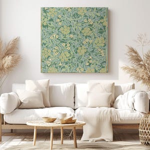 Può includere: Un'opera d'arte quadrata su tela con un motivo botanico nei toni del verde, blu e crema. L'opera è esposta sopra un divano bianco con cuscini beige e un tavolino in legno, creando un'atmosfera accogliente nel soggiorno.