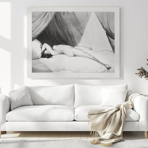Peut inclure: Impression en noir et blanc d'une figure allong&eacute;e sur un lit, avec des draperies. L'&oelig;uvre est encadr&eacute;e et accroch&eacute;e au-dessus d'un canap&eacute; blanc avec des coussins et une couverture beige. Une table d'appoint avec une lampe et un vase avec des plantes s&eacute;ch&eacute;es compl&egrave;tent la sc&egrave;ne.