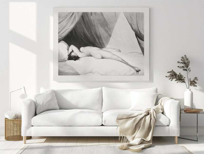 Peut inclure: Impression en noir et blanc d'une figure allong&eacute;e sur un lit, avec des draperies. L'&oelig;uvre est encadr&eacute;e et accroch&eacute;e au-dessus d'un canap&eacute; blanc avec des coussins et une couverture beige. Une table d'appoint avec une lampe et un vase avec des plantes s&eacute;ch&eacute;es compl&egrave;tent la sc&egrave;ne.