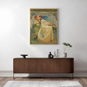 Peut inclure: Une affiche encadrée représentant une femme en robe longue, avec des motifs floraux et le texte "PRINCESS HYACINTH". L'œuvre est dans un cadre doré, au-dessus d'un meuble en bois avec des objets décoratifs.