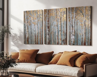 May include: Three-panel wall art featuring a forest scene with birch trees. The artwork has a muted color palette of blue, white, and gold. The trees have white bark and gold-colored leaves. The art is displayed above a white sofa with orange-brown pillows.