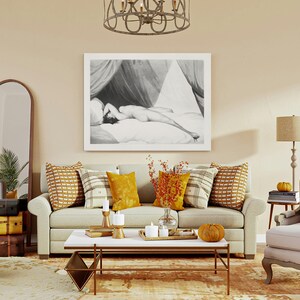 Peut inclure: Int&eacute;rieur de salon avec un canap&eacute; beige, des coussins d&eacute;coratifs et une table basse. Une grande &oelig;uvre d'art en noir et blanc encadr&eacute;e est accroch&eacute;e au-dessus du canap&eacute;. Un miroir et des valises vintage empil&eacute;es sont &agrave; gauche. Une lampe et un fauteuil sont &agrave; droite.