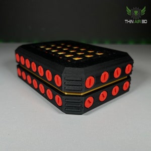May include: A black and yellow 3D printed box with a grid pattern on the top and red buttons around the sides. The box is closed and the text "THIN AIR 3D" is visible on the top.