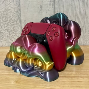 May include: A 3D printed, rainbow-coloured cloud-shaped stand holds a red video game controller. The stand has a metallic sheen and is made of plastic.