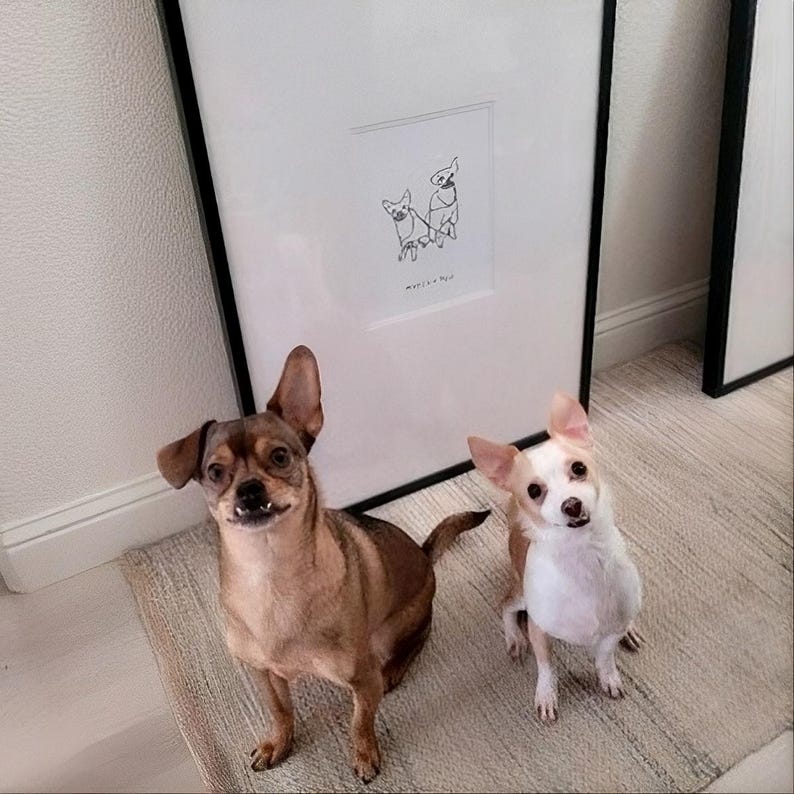 May include: A framed black and white line art print featuring a drawing of two small dogs connected by a leash. The artwork is displayed in a simple black frame. Below the drawing, the text reads "MY LITTLE DOGS" in a clean, minimalist font.