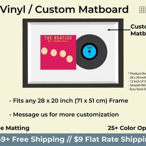 May include: A black framed picture with a white mount and a vinyl record inside. The record is black with a blue label that says "Capitol". The record is next to a red album cover with the text "THE BEATLES" in yellow. The album cover has four white circles on it. The image is titled "LP Vinyl / Custom Matboard" and includes the text "Custom Matboard" and "Fits any 28 x 20 inch (71 x 51 cm) Frame".