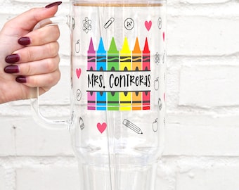 Puede incluir: Un vaso de vidrio transparente con asa, tapa de bambú y pajita de vidrio. El exterior presenta un gráfico colorido de crayones sobre el texto "MRS. CONTRERAS" y pequeños iconos que incluyen corazones, manzanas, lápices y átomos en la superficie.