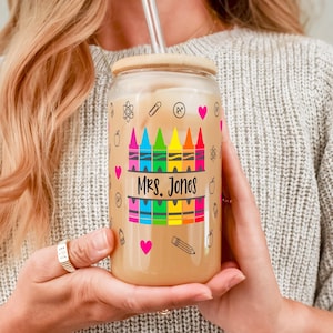 May include: A clear glass tumbler with a brown lid and a straw. The tumbler has a design of colorful crayons, a heart, and the text "MRS. JONES".