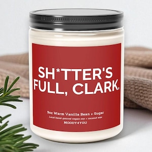 May include: A 9oz candle in a clear glass jar with a black lid and a red label. The label features white text that reads SH*TTER'S FULL, CLARK. and Warm Vanilla Bean + Sugar. The brand name MOODY4YOU is printed at the bottom of the red label.