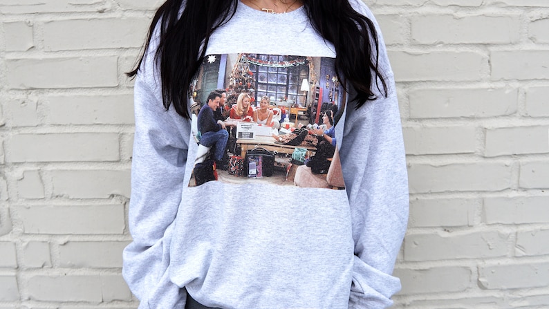 May include: A gray sweatshirt with a printed image of the six main characters from the TV show "Friends" gathered around a table with a Christmas tree in the background.