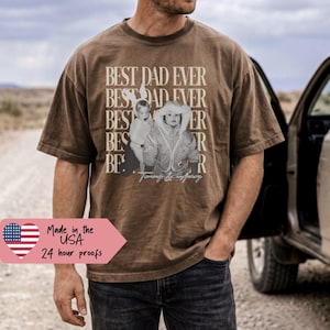 May include: Brown t-shirt with the text "BEST DAD EVER" in a stacked design, featuring a sepia-toned photo of a child. The shirt is worn by a person standing next to a vehicle. The shirt also has the text "Made in the USA" and "24 hour proofs".