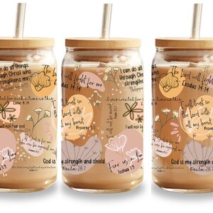 May include: Glass tumbler with a bamboo lid and straw, featuring a floral design and inspirational quotes in various fonts. The tumbler has a light brown beverage inside, with a beige and pink color palette.