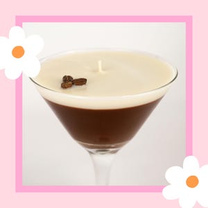 May include: A white and brown coffee-themed candle in a martini glass. The candle has a white top layer and a brown bottom layer. There are coffee beans on top of the white layer.