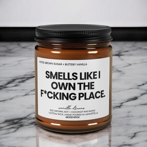 May include: A brown glass jar candle with a black lid. The label reads "Smells Like I Own The F*cking Place." Additional text includes "Brown Sugar + Buttery Vanilla" and "Vanilla Dreams." The candle is 255g and made with soy and coconut wax.