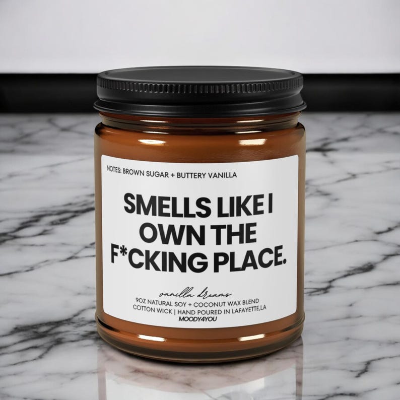 May include: A brown glass jar candle with a black lid. The label reads "Smells Like I Own The F*cking Place." Additional text includes "Brown Sugar + Buttery Vanilla" and "Vanilla Dreams." The candle is 255g and made with soy and coconut wax.