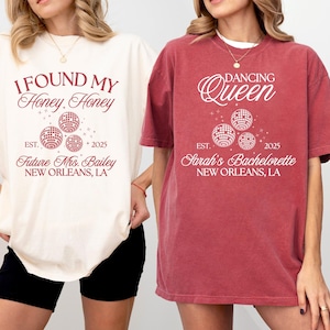 K&ouml;nnte beinhalten: Zwei T-Shirts, eines cremefarben und eines rot, mit wei&szlig;em Text und Discokugel-Grafiken. Das cremefarbene Shirt tr&auml;gt die Aufschrift "I FOUND MY Honey Honey" und "Future Mrs. Bailey, New Orleans, LA". Das rote Shirt tr&auml;gt die Aufschrift "DANCING Queen" und "Sarah's Bachelorette, New Orleans, LA".