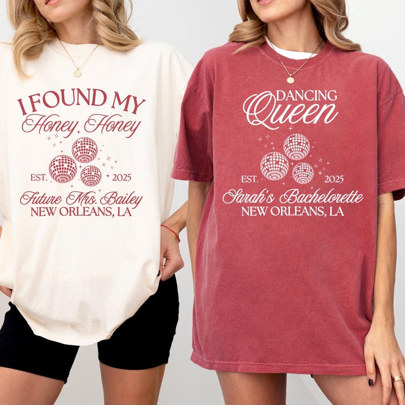 K&ouml;nnte beinhalten: Zwei T-Shirts, eines cremefarben und eines rot, mit wei&szlig;em Text und Discokugel-Grafiken. Das cremefarbene Shirt tr&auml;gt die Aufschrift "I FOUND MY Honey Honey" und "Future Mrs. Bailey, New Orleans, LA". Das rote Shirt tr&auml;gt die Aufschrift "DANCING Queen" und "Sarah's Bachelorette, New Orleans, LA".