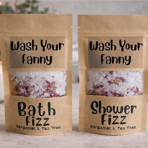 Puede incluir: Dos bolsas de papel marrón con ventanas transparentes, llenas de productos de baño. El texto "Wash Your Fanny" está encima de la ventana. Debajo, uno dice "Bath Fizz" y el otro "Shower Fizz". Ambos dicen "Bergamot & Tea Tree".