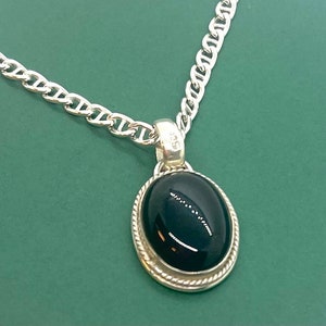 Op de afbeelding: Een zilveren ketting met een hanger met een zwarte ovale edelsteen in een zilveren zetting.