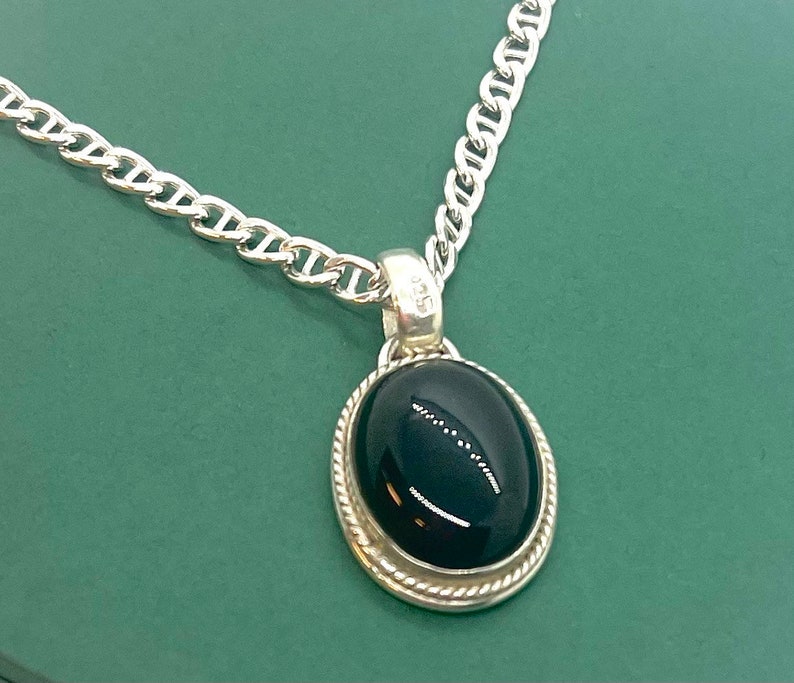 Op de afbeelding: Een zilveren ketting met een hanger met een zwarte ovale edelsteen in een zilveren zetting.