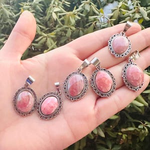 May include: Five silver oval pendants with pink and white gemstone inserts. Each pendant has a decorative silver border.