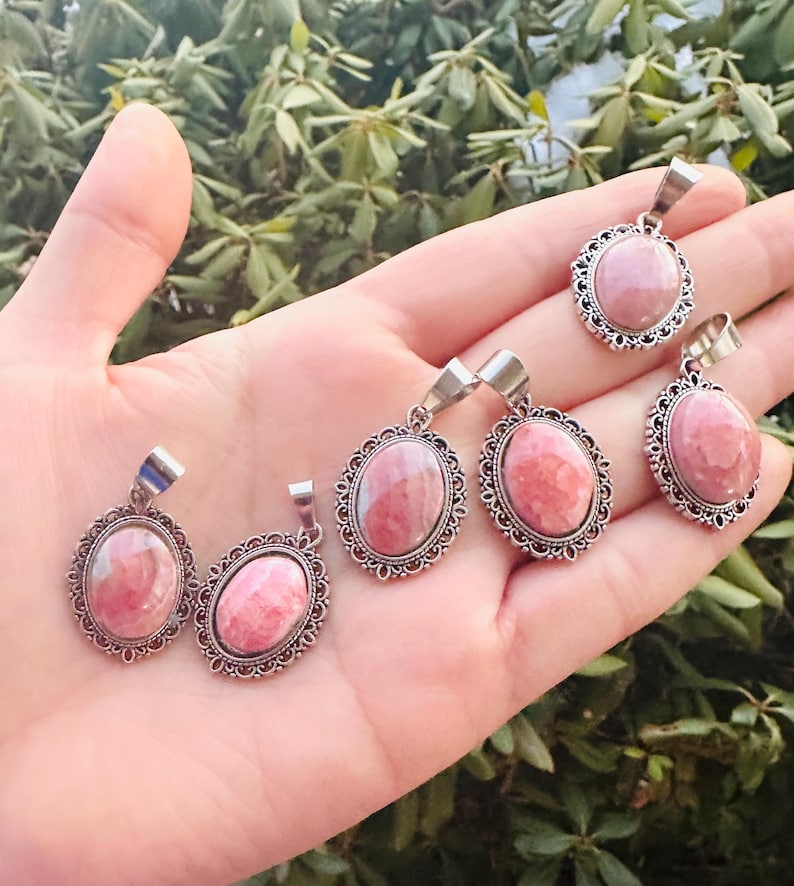 May include: Five silver oval pendants with pink and white gemstone inserts. Each pendant has a decorative silver border.