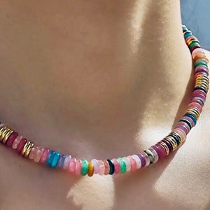 May include: A colorful beaded necklace with gold accents. The beads are made of various gemstones in shades of pink, purple, green, and blue.
