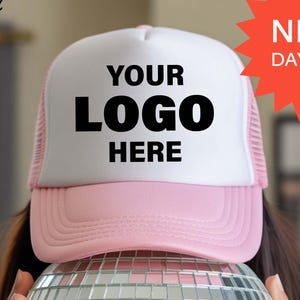 May include: A pink and white trucker hat with the text "YOUR LOGO HERE" in black. The hat is placed on top of a mirrored disco ball. The image also includes a red starburst with the text "NEXT DAY SHIP". The Shining Pearl Clothing logo is in the upper left corner.