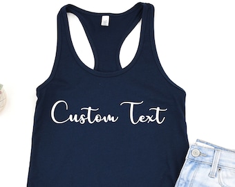 May include: A navy blue tank top with the text "Custom Text" in white lettering. The tank top is laying flat on a white surface next to a pair of light blue denim shorts.