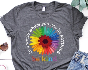 May include: A dark gray t-shirt with a rainbow flower graphic and the text "In a world where you can be anything be kind".